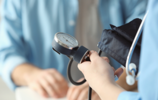 A home care worker in blue scrubs measures a patient's blood pressure with a sphygmomanometer, focusing on health monitoring and medical care.
