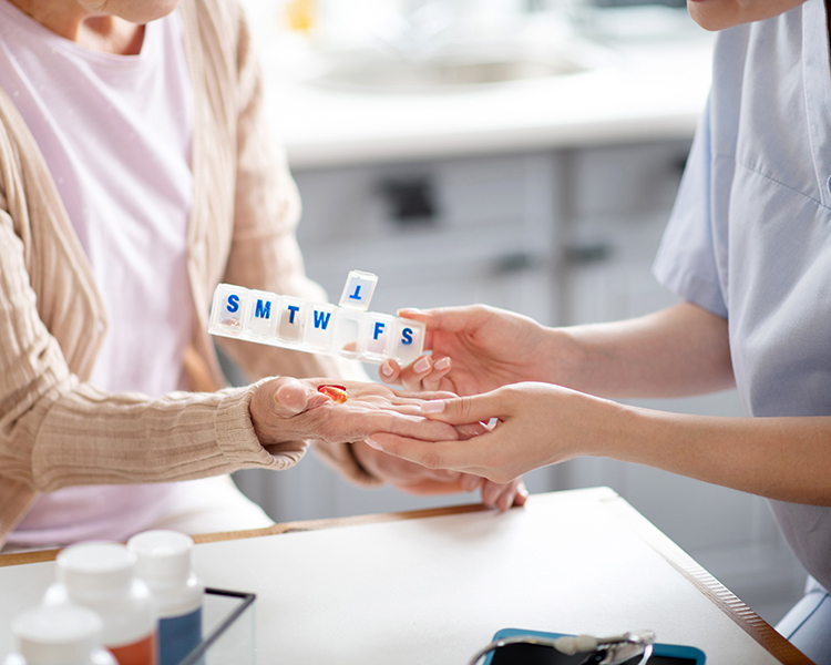 An HMC HomeCare caregiver is dispensing medicine to an elderly client.