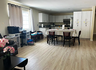 Spacious dining and kitchen area at HMC Care Home in Honolulu, featuring shared seating, white cabinetry, and a warm, homelike environment for residents.