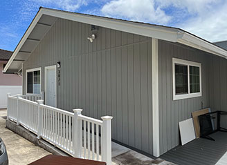 Exterior view of HMC Care Home in Honolulu with ramp access, gray siding, and white railing, offering a welcoming entrance for residential senior care.
