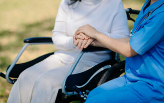 caregiver holding senior patient hand in wheelchair outdoor setting, in-home care support, elderly assistance, mobility care, compassionate senior care services